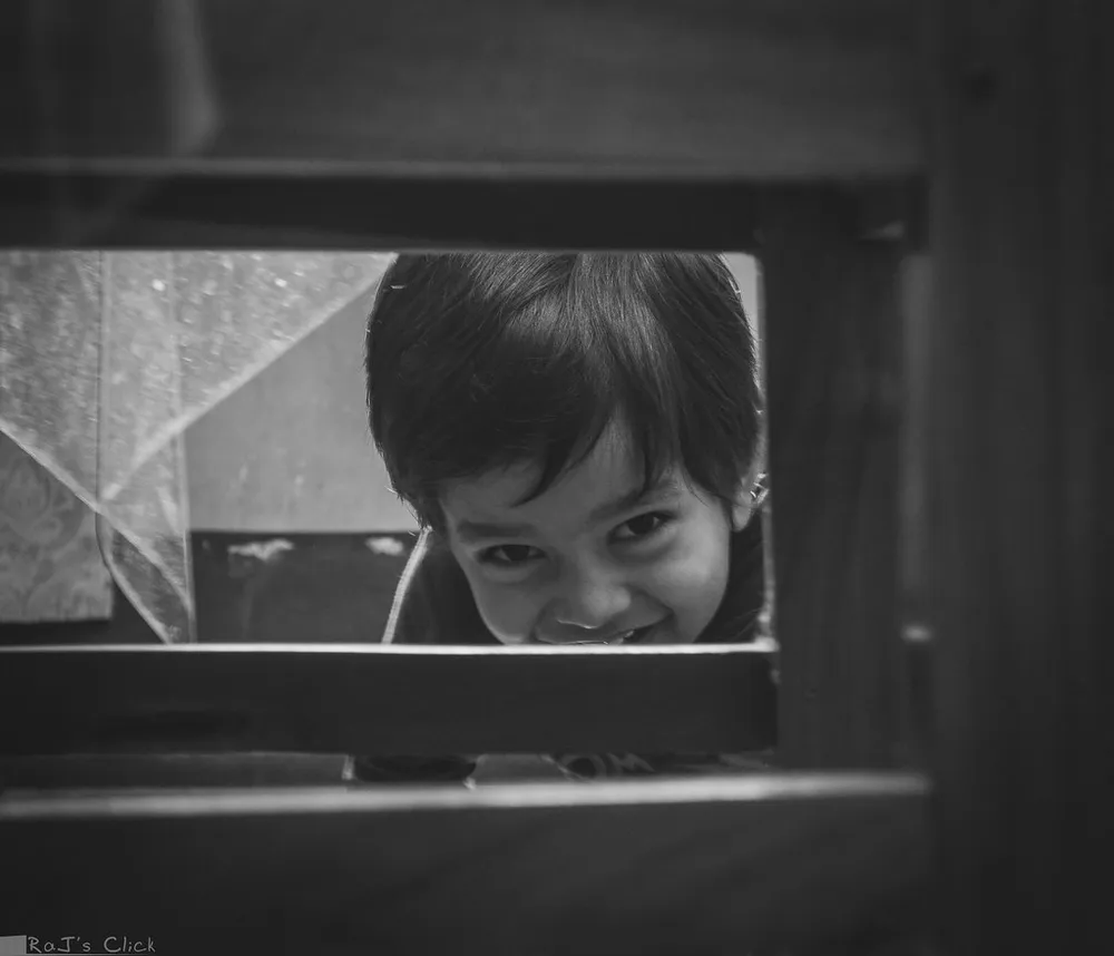 Black-and-white portrait of a child smiling through a window frame
